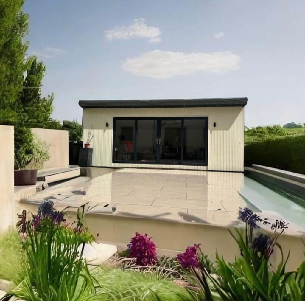 Modern garden room with large patio and surrounding greenery under clear sky.