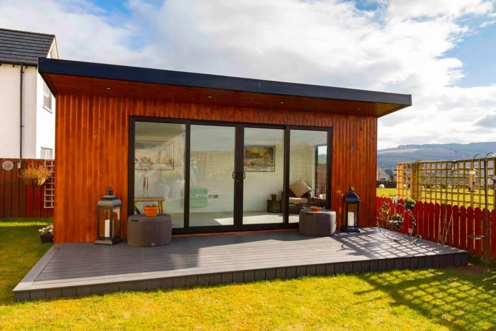 Modern wooden garden room with glass doors and outdoor seating on a sunny day.