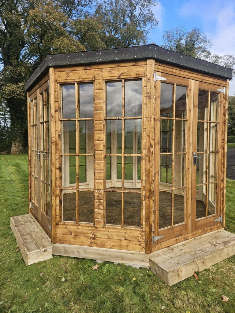 Wooden gazebo with large windows in a grassy yard.