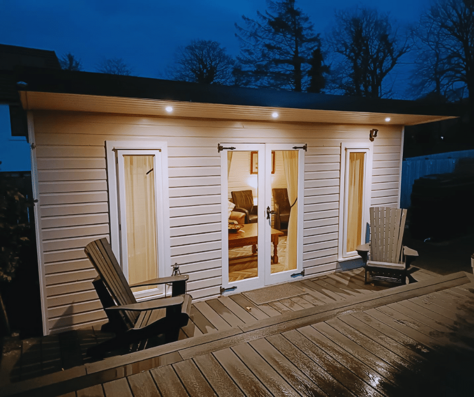Outdoor evening view of a lit family entertainment room with Adirondack chairs on a wooden deck.