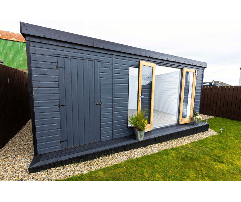 Modern blue hobby room with large windows and wooden door, surrounded by grass and gravel pathway.