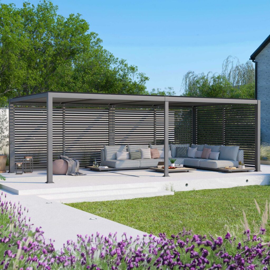 Modern outdoor pergola with gray seating, surrounded by greenery and purple flowers, under a clear blue sky.