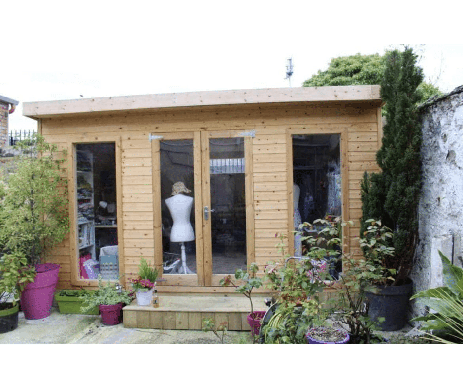 Wooden sewing room with large windows, surrounded by greenery and various potted plants.