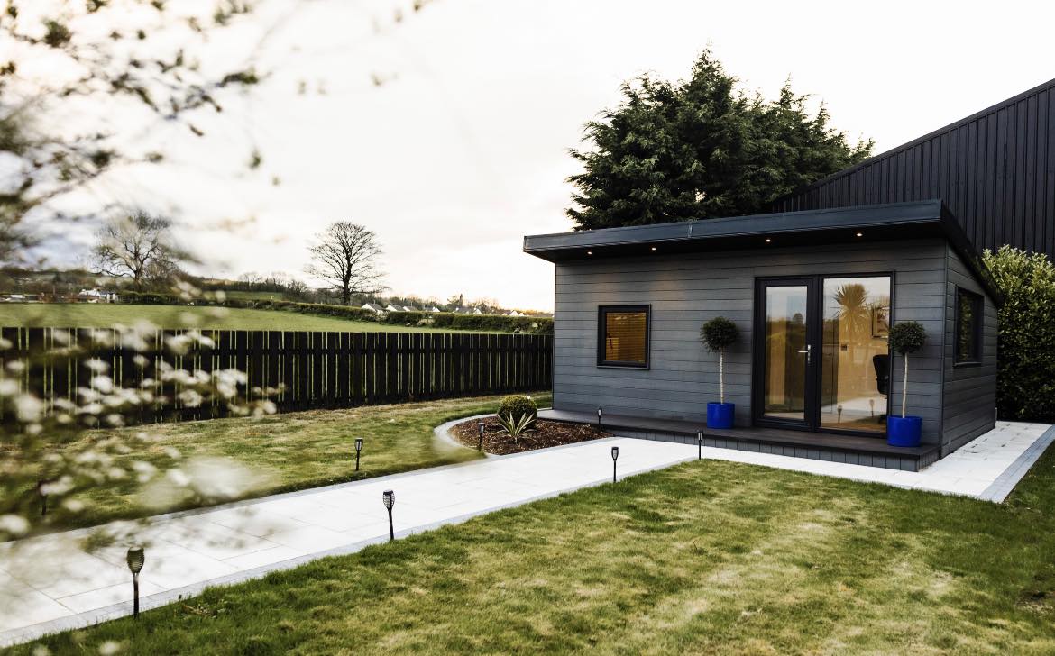 Modern garden office with large windows, surrounded by a lush lawn and trees, featuring a contemporary design.