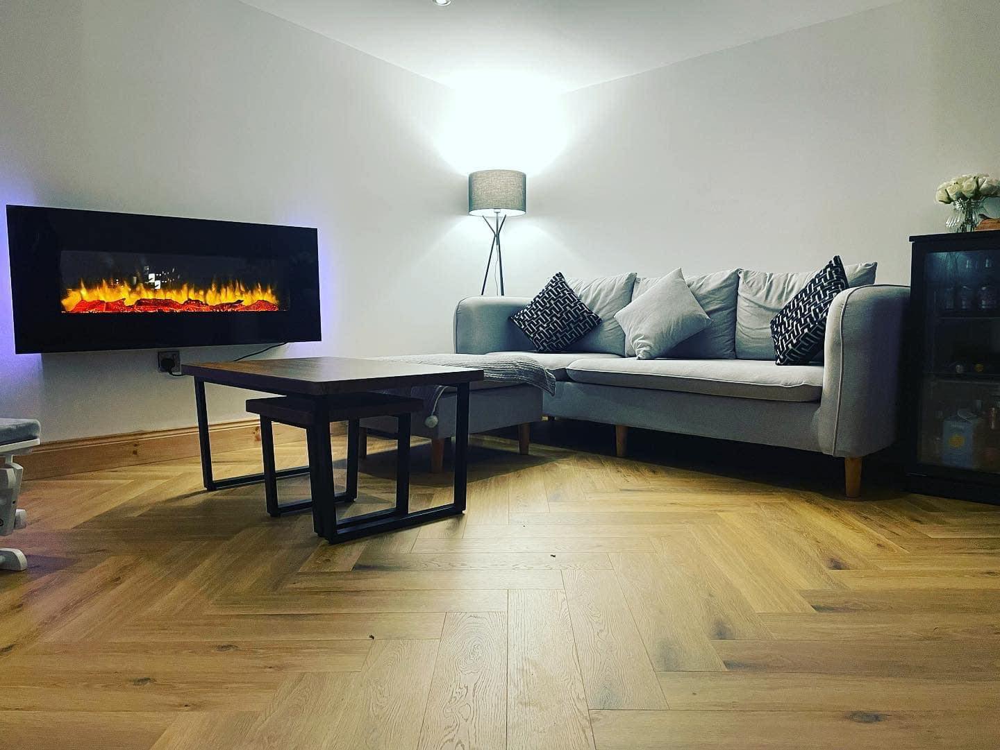 Modern living room with a wall-mounted electric fireplace, gray sofa, black and white cushions, and wooden floor.