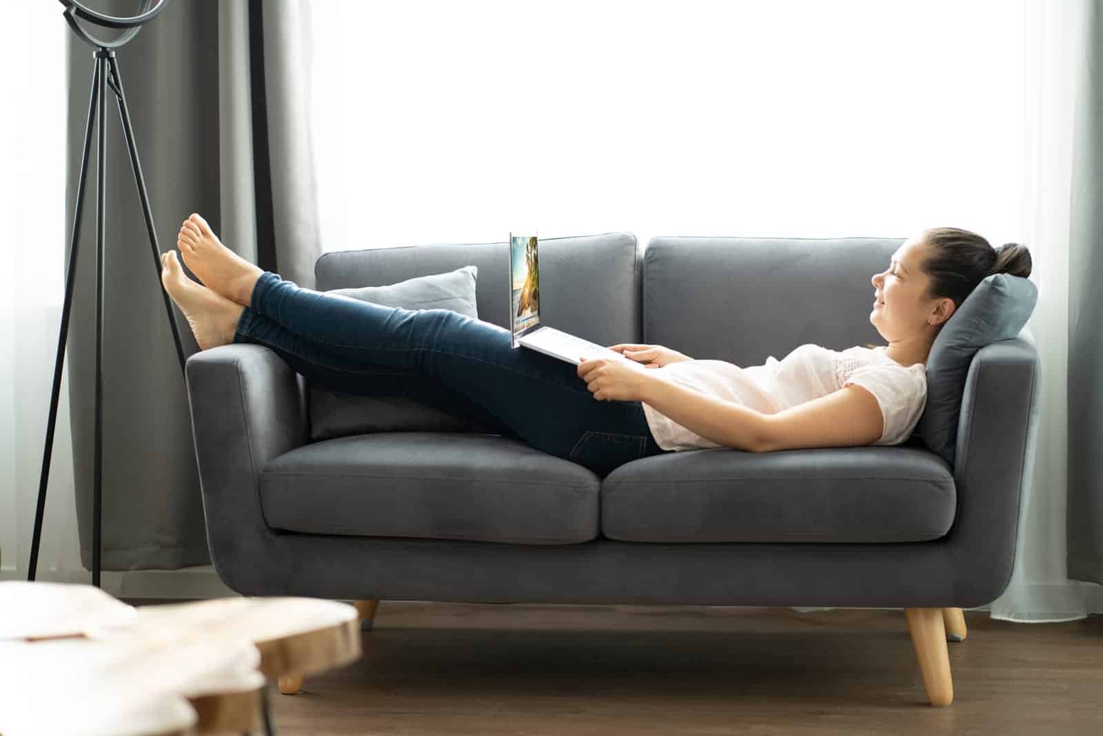 Woman relaxing on a gray couch with a laptop on her lap.